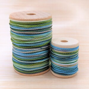 May include: Two spools of green, blue, and white striped embroidery floss wound on wooden spools.