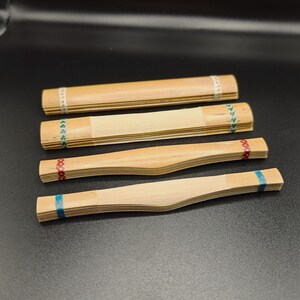 May include: Four wooden reeds for a musical instrument, each with a different colored ribbon at the end. The reeds are stacked on top of each other, with the blue ribboned reed at the bottom and the white ribboned reed at the top.