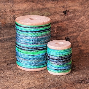 May include: Two spools of colourful thread wound on wooden bobbins. The thread is a mix of blue, green, and black.