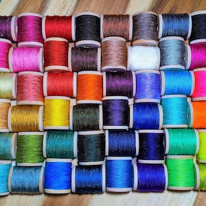May include: A collection of 42 spools of thread in various colors, including red, blue, green, yellow, orange, purple, and brown. The spools are arranged in a grid pattern on a wooden surface.