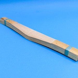 May include: A stack of thin wooden slats bound together with blue tape. The slats are curved and arranged in a fan shape.