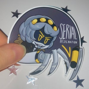 Peut inclure: Autocollant rond représentant un personnage de dessin animé avec des cheveux gris, des accents jaunes et un corps robotique en forme d'araignée. Le texte "SERIAL DESIGNATION" est présent, entouré d'étoiles argentées.