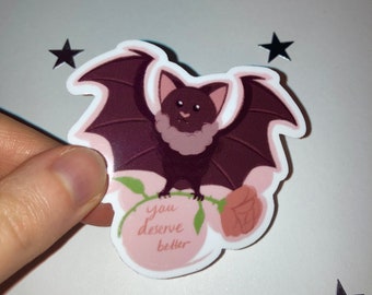 May include: A sticker featuring a cartoon bat with outstretched wings, perched on a rose. The bat is dark brown with a light pink face and wings. The sticker has the text "you deserve better" in a pink circle.