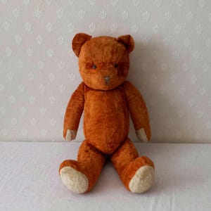 Op de afbeelding: Een bruine teddybeer met een pluche, donzige textuur. De beer zit met gekruiste benen en heeft een eenvoudig, gestikt gezicht.