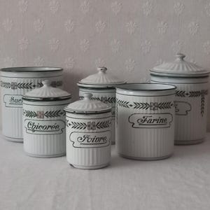 Puede incluir: Un conjunto de seis botes de cocina de cerámica blanca con tapas. Cada bote tiene un borde negro y está decorado con un diseño floral negro y etiquetas de texto. Las etiquetas incluyen "Sucre", "Chicoree", "Poivre" y "Farine".