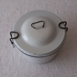 以下が含まれることがあります： 金属製の取っ手が2つと、金属製の取っ手付きの蓋が付いた白いエナメル製のランチボックスです。