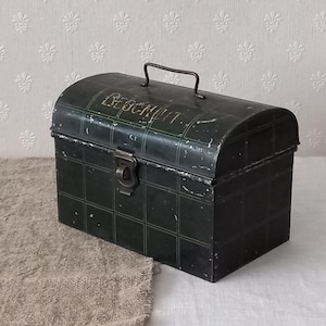 Könnte beinhalten: Eine dunkelgrüne Metallbox im Vintage-Stil mit gewölbtem Deckel und Griff. Die Box hat ein Gittermuster und das Wort "BESCHRIFT" ist auf der Oberseite geschrieben. Sie hat einen Schnappverschluss und Gebrauchsspuren.