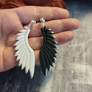 Pu&ograve; includere: Un paio di orecchini pendenti con un design ad ala d'angelo in bianco e nero. Le ali sono realizzate in materiale testurizzato e hanno una finitura argentata.