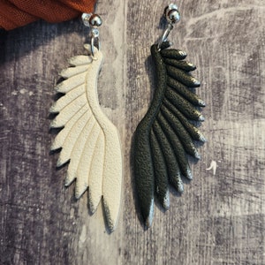 Pu&ograve; includere: Un paio di orecchini pendenti con un design ad ala bianco e nero. Le ali sono realizzate in pasta polimerica e hanno una finitura testurizzata.