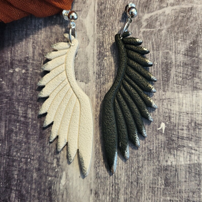 Pu&ograve; includere: Un paio di orecchini pendenti con un design ad ala bianco e nero. Le ali sono realizzate in pasta polimerica e hanno una finitura testurizzata.