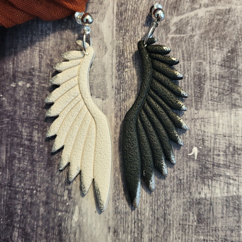 Pu&ograve; includere: Un paio di orecchini pendenti con un design ad ala bianco e nero. Le ali sono realizzate in pasta polimerica e hanno una finitura testurizzata.