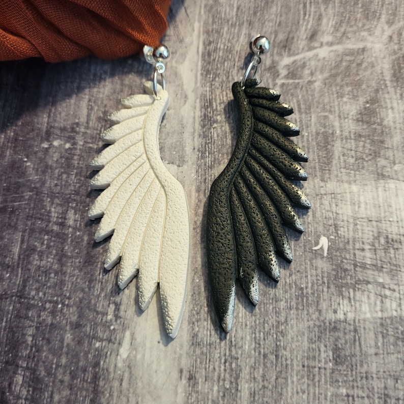Pu&ograve; includere: Un paio di orecchini con un design ad ala bianco e nero. Le ali sono realizzate in un materiale strutturato e hanno un aspetto leggermente 3D.