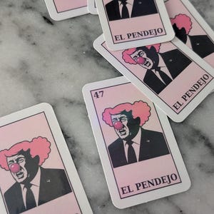 May include: A collection of playing cards featuring a caricature of a man with a clown nose and pink hair. The cards have the number 47 and the text "EL PENDEJO" printed on them. The background is a light pink color.
