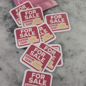 Może przedstawiać: Kolekcja czerwono-białych naklejek z napisami "FOR SALE" i "SUPREME COURT". Naklejki przedstawiają grafikę budynku. Niektóre naklejki są rozrzucone, a niektóre wciąż w opakowaniu.