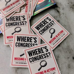 May include: Rectangular white stickers with a red border and black text. The stickers read "WHERE'S CONGRESS?" with a magnifying glass graphic. Below, it says "MISSING IN ACTION!" and "CIVIC ACCOUNTABILITY - EST. 2026".