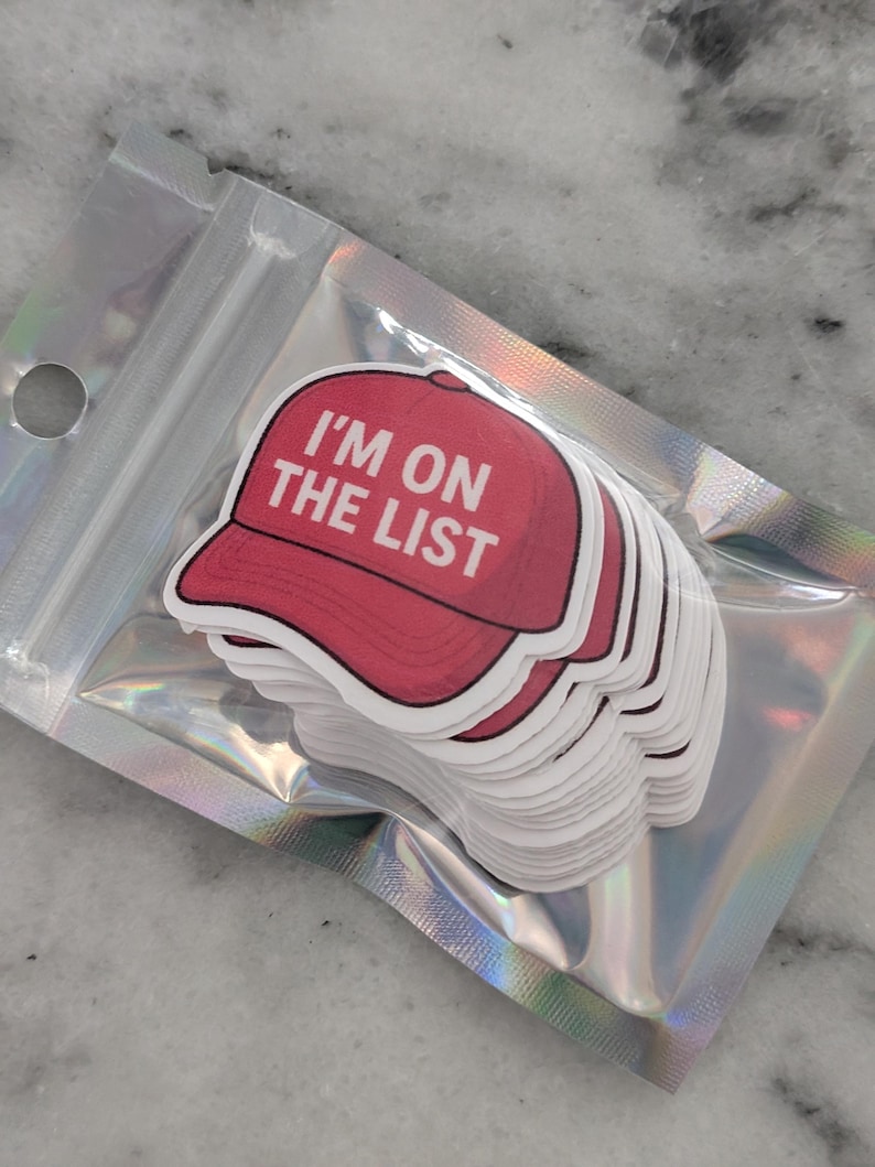 May include: A stack of stickers featuring a red baseball cap design with the text "I'M ON THE LIST" in white. The stickers are packaged in a clear, iridescent pouch.