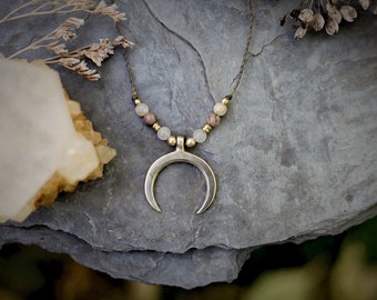 Puede incluir: Un collar con un colgante de media luna, un cordón marrón y cuentas beige y marrones.