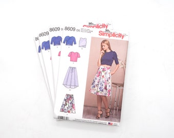 May include: A sewing pattern for a crop top and skirt. The pattern is for sizes 4-12, 30-34, 36-40. The pattern is from Simplicity and is for their 90th anniversary. The pattern shows a model wearing a blue crop top and a floral skirt.