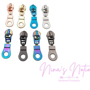 May include: Assortment of zipper pulls in various colors, including gold, silver, blue, and iridescent. The zipper pulls are made of metal and have a loop at the top for attaching to a zipper.