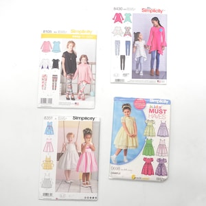Puede incluir: Cuatro patrones de costura diferentes para ropa de niños. Los patrones son de Simplicity y presentan una variedad de estilos, incluyendo vestidos, blusas y leggings. Los patrones están todos en color y presentan ilustraciones de las prendas terminadas.