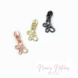 Puede incluir: Tres tiradores de cremallera con dijes de mariposa. Los dijes son de oro, oro rosa y negro.