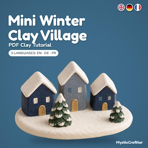 May include: A PDF clay tutorial titled Mini Winter Clay Village featuring three small houses in dark blue and grey with white snow-covered roofs, gold doors, and two green pine trees on a round white base, available in English, German, and French.