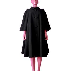 May include: A black vintage cape coat with a flared silhouette. The coat features a round collar, three large buttons down the front, and three-quarter length sleeves. The coat is displayed on a mannequin.
