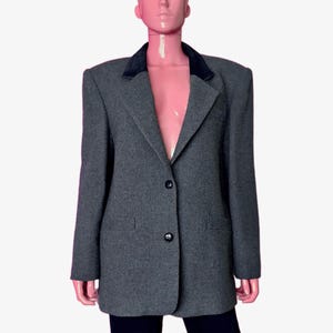 May include: A gray blazer with a black velvet collar and two black buttons. The blazer has a textured pattern and two front pockets. The blazer is displayed on a mannequin.