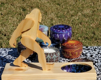 May include: Wooden Bigfoot figurine standing on a wooden base with a mirror. The base also has a red Sharpie marker on it. The figurine is surrounded by several small, round, colorful candle tins.