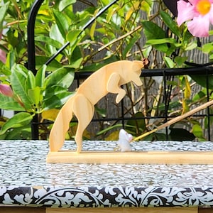 May include: A wooden fox figurine jumping over a wooden mouse figurine on a wooden incense holder. The holder is on a black and white patterned surface.