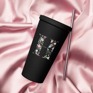 Puede incluir: Vaso reutilizable negro con un diseño de letra H floral. El vaso tiene una tapa y una pajita plateada.