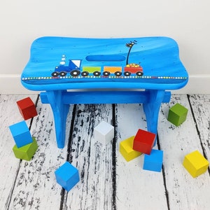 May include: A blue wooden step stool with a painted design of a train and a giraffe. The stool is surrounded by colorful wooden blocks.