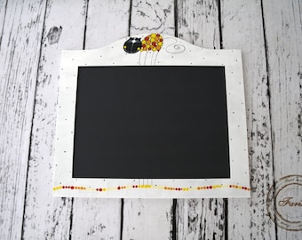 May include: White chalkboard with a black cat holding yellow and orange balloons painted on the top. The chalkboard has a white frame with a dotted pattern and a yellow and orange dotted border.