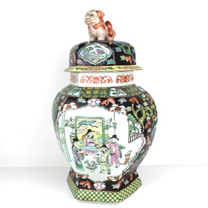 Peut inclure: Un grand pot octogonal en porcelaine avec un couvercle. Le pot est décoré d'un fond noir et de motifs floraux et figuratifs colorés. Le couvercle est orné d'un petit lion en porcelaine tridimensionnel.