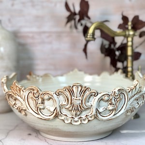 Puede incluir: Un cuenco de cerámica blanco con un diseño marrón ornamentado y elevado alrededor del borde. El cuenco está sobre una superficie blanca.