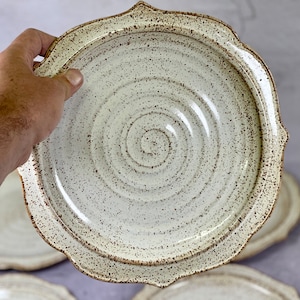 May include: A set of four white ceramic dinner plates with a speckled glaze and scalloped edges. The plates have a subtle swirl pattern in the center.