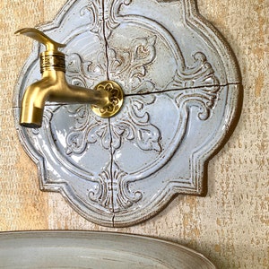 Puede incluir: Un lavabo de cerámica montado en la pared con un diseño decorativo de azulejos azules y blancos. El lavabo tiene un grifo de latón y una cuenca de cerámica a juego.