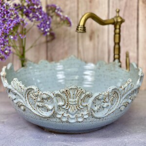 Puede incluir: Un lavabo de cer&aacute;mica azul claro con un dise&ntilde;o ornamentado y elevado alrededor del borde. El lavabo est&aacute; hecho en un estilo r&uacute;stico y tiene un esmalte moteado.