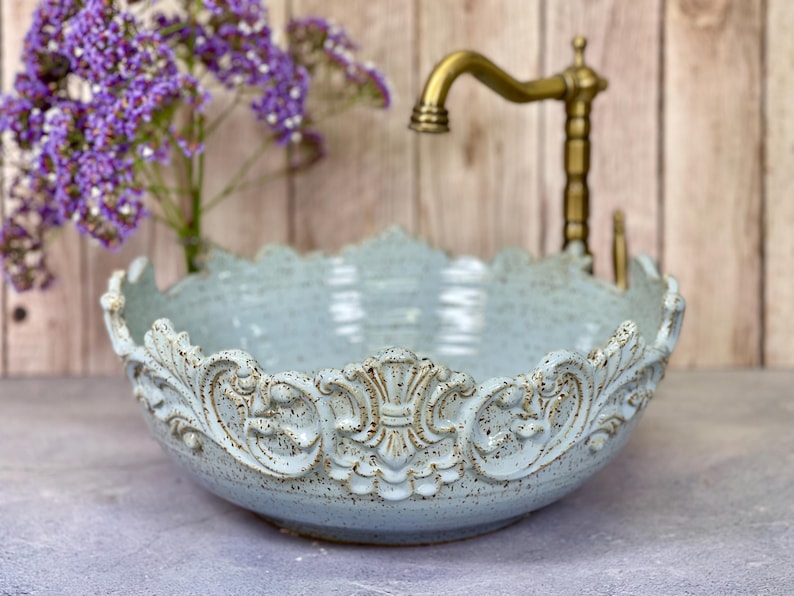 Puede incluir: Un lavabo de cer&aacute;mica azul claro con un dise&ntilde;o ornamentado y elevado alrededor del borde. El lavabo est&aacute; hecho en un estilo r&uacute;stico y tiene un esmalte moteado.