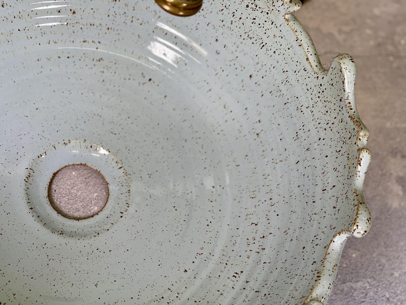 Puede incluir: Un lavabo de cer&aacute;mica azul claro con un esmalte moteado y un borde festoneado. El lavabo tiene un peque&ntilde;o agujero de drenaje en el centro.