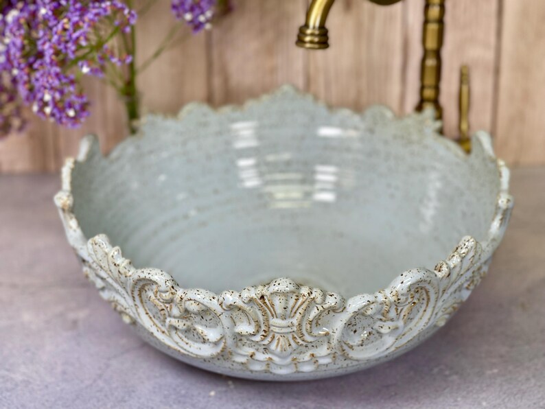 Puede incluir: Un lavabo de cer&aacute;mica azul claro con un borde decorativo y ornamentado. El lavabo es redondo y tiene un acabado liso y brillante.