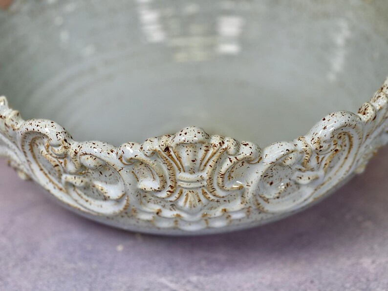 Puede incluir: Un cuenco de cer&aacute;mica blanca con un borde decorativo y ornamentado. El borde tiene un dise&ntilde;o elevado y detallado con un glaseado marr&oacute;n moteado.