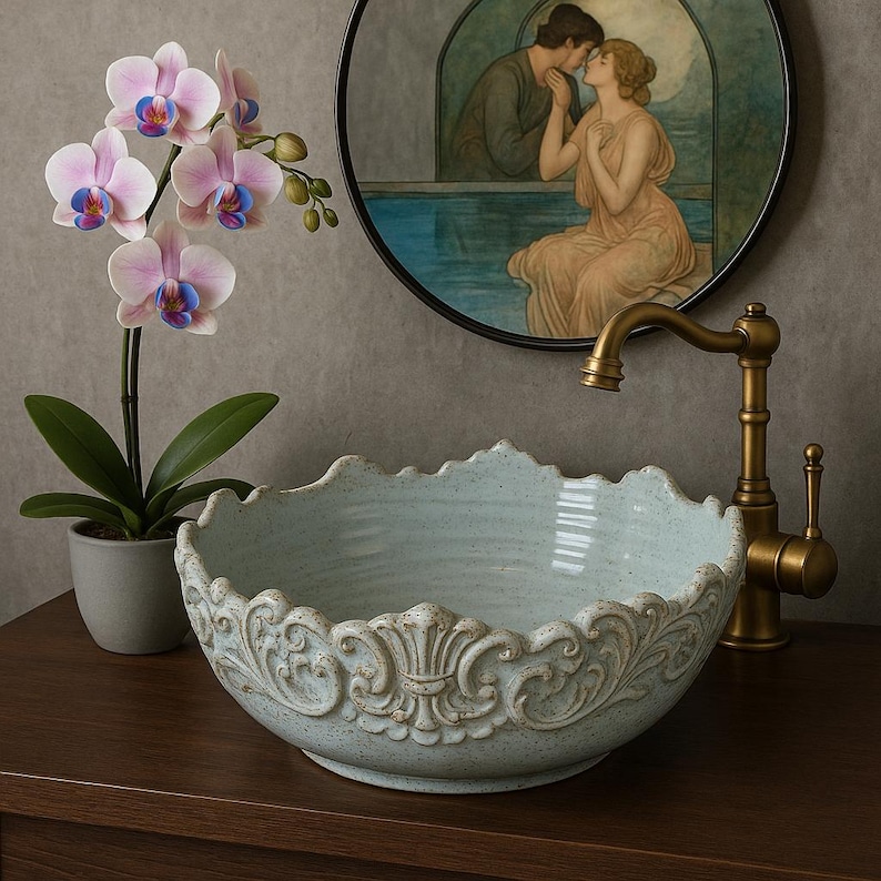 Puede incluir: Un lavabo de ba&ntilde;o de cer&aacute;mica azul claro con un dise&ntilde;o ornamentado y decorativo alrededor del borde. El lavabo est&aacute; sobre una encimera de madera con un grifo dorado.