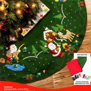 Peut inclure: Un kit de jupe de sapin de Noël en feutrine verte avec des scènes brodées et perlées représentant le Père Noël pêchant, campant et interagissant avec un cerf près d'un chalet. Le kit contient de la feutrine imprimée, du fil, des perles et aiguilles.