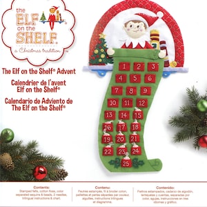 Peut inclure: Un kit de loisirs créatifs Bucilla pour calendrier de l'avent Elf on the Shelf, présentant une chaussette en feutrine verte avec des poches rouges numérotées de 1 à 25. L'emballage montre le produit fini, du texte et la liste des composants.