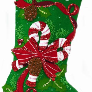May include: A green felt Christmas stocking featuring the name Stephanie embroidered in white script. The stocking is decorated with red and white sequined candy canes, a red bow, brown pinecones, green holly leaves, and red berries.