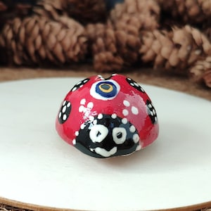 May include: A red ladybird ornament with black spots and a smiling face. The ladybird has a glossy finish and is set on a white wooden circle. Decorative item for home decor.