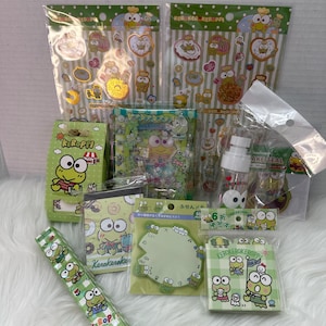 May include: A collection of Keroppi-themed stationery and accessories. The items include stickers, memo pads, a roll of decorative tape, and a small spray bottle. The products feature the Keroppi character in various poses and designs, with green and white color schemes.