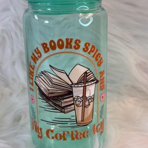 May include: A turquoise glass water bottle with a white sticker that says "I like my books spicy and my coffee icy". The sticker features a stack of books and a glass of iced coffee with a straw.