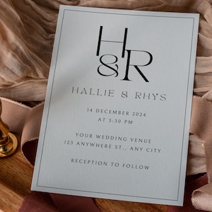 May include: A light blue wedding invitation with black text. The invitation features the couple's initials, "H&R", and their names, "Hallie & Rhys". The date and time of the wedding are listed as "14 December 2024 at 3:30 PM". The wedding venue is listed as "Your Wedding Venue, 123 Anywhere St., Any City". The invitation concludes with "Reception to Follow".